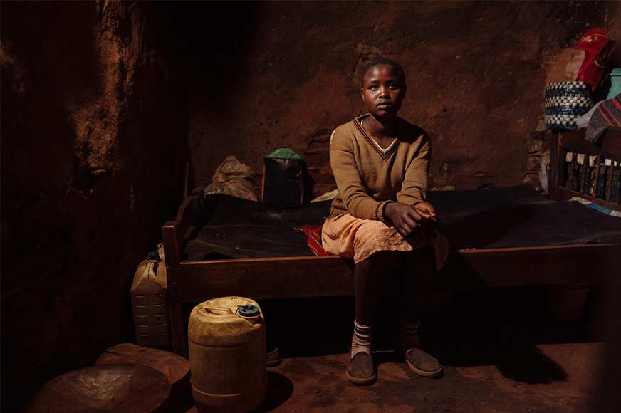 Lente, 12 years old, sits on her bed in a dimly lit room. She takes part in sessions that educate about the consequences of FGM and child marriage.