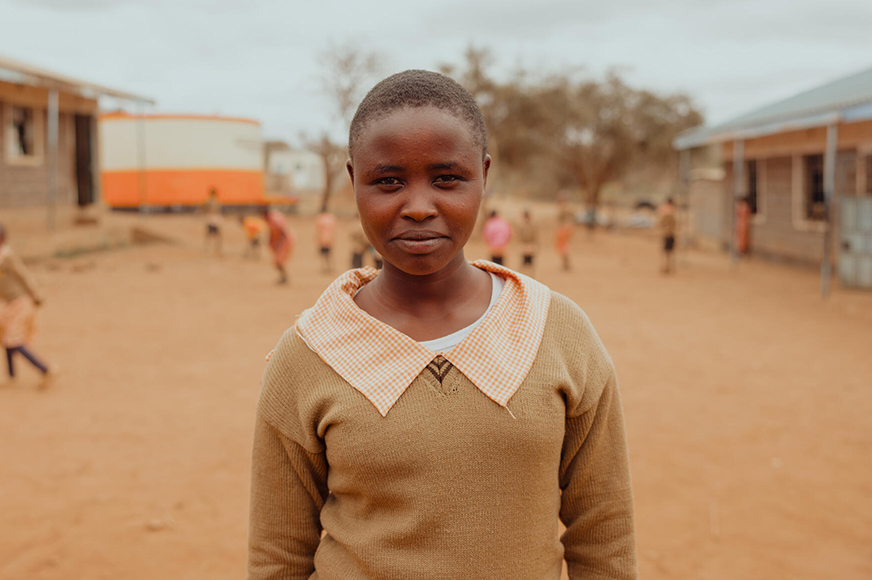 Lente, standing in the schoolyard. She says she has learned about her rights and how to report thanks to Peninah.