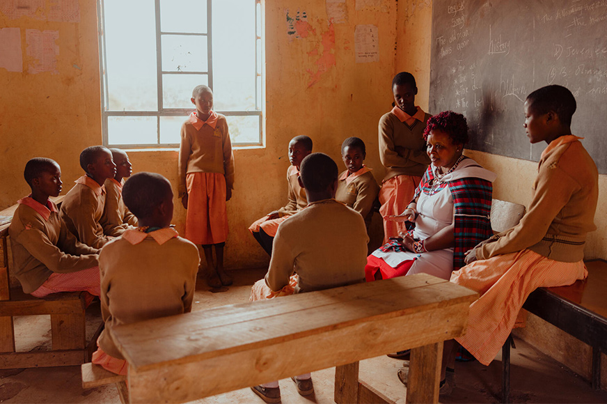 Peninah is in a classroom surrounded by school girls. She holds information sessions at the local school to tell others about girls rights, the dangers of FGM and child marriage.