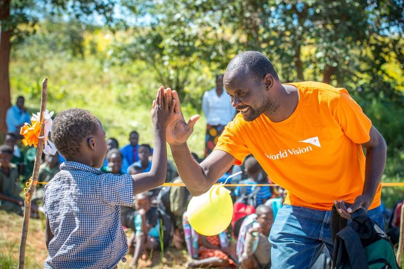 World Vision Volunteer high fiving a little boy a job well done, smiling