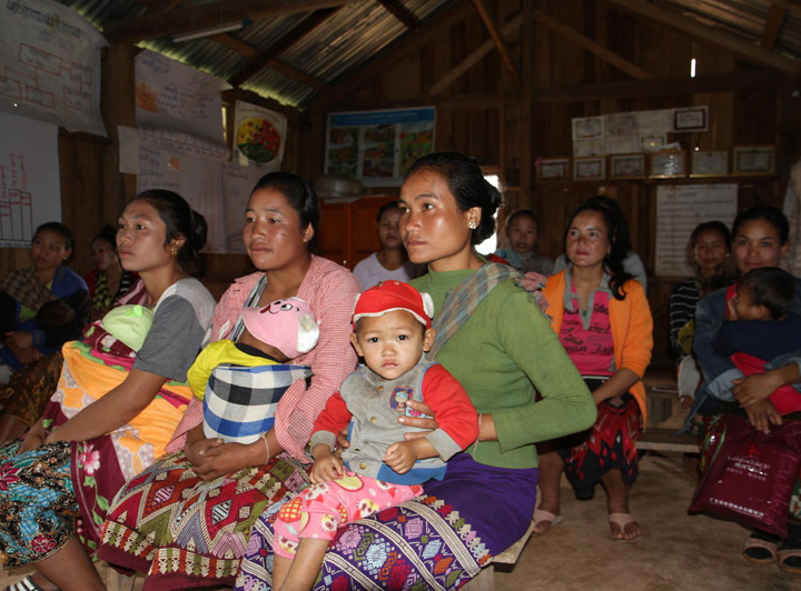 A group of mothers attend health training in their community in Laos. Their babies sit on their laps.