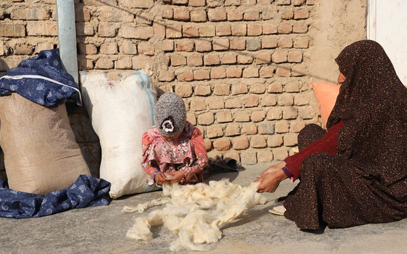 A woman and small girl sit on the ground, cleaning fluff to spill and sell for a little income.