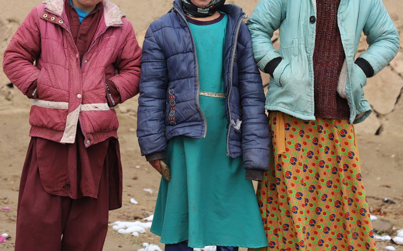 Cropped image of three school-age children in winter coats, standing outdoors.