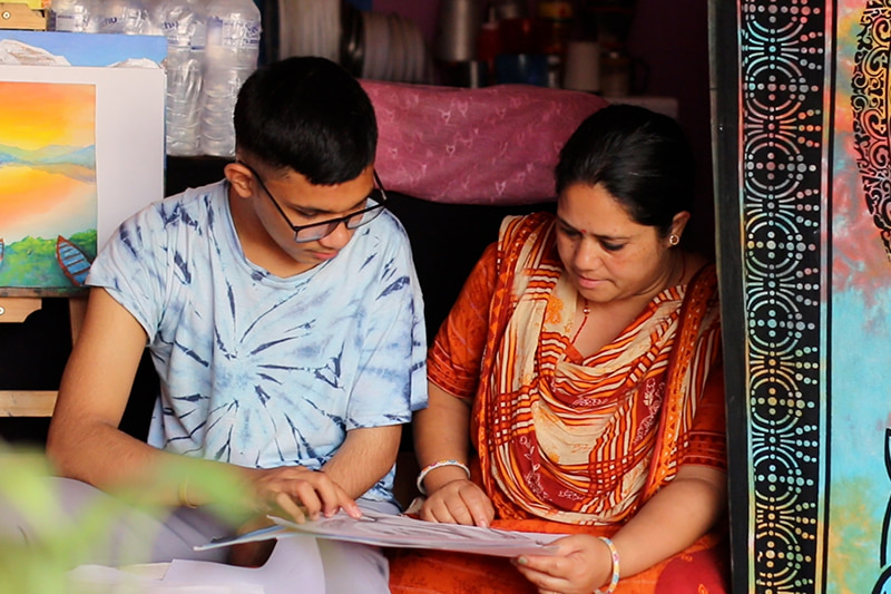 Rahul and his mother sit side-by-side, looking at one of his drawings.