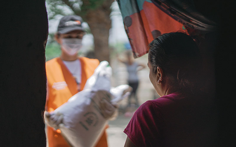 A mother in Honduras opens the door to a World Vision worker who is carrying a bag of seeds.