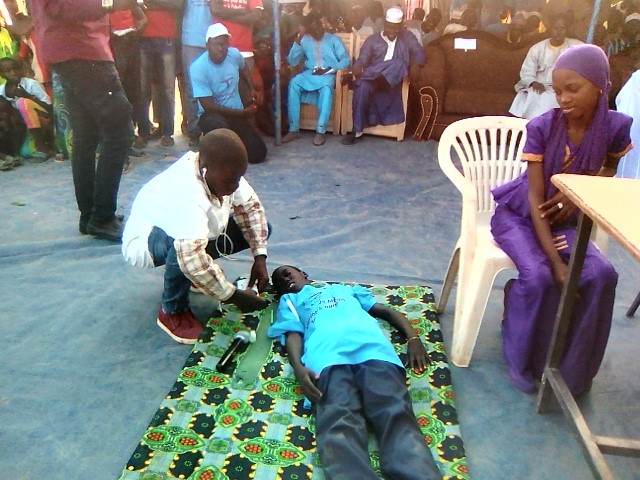 A crowd watch as a boy check on a boy that is laying on the floor.