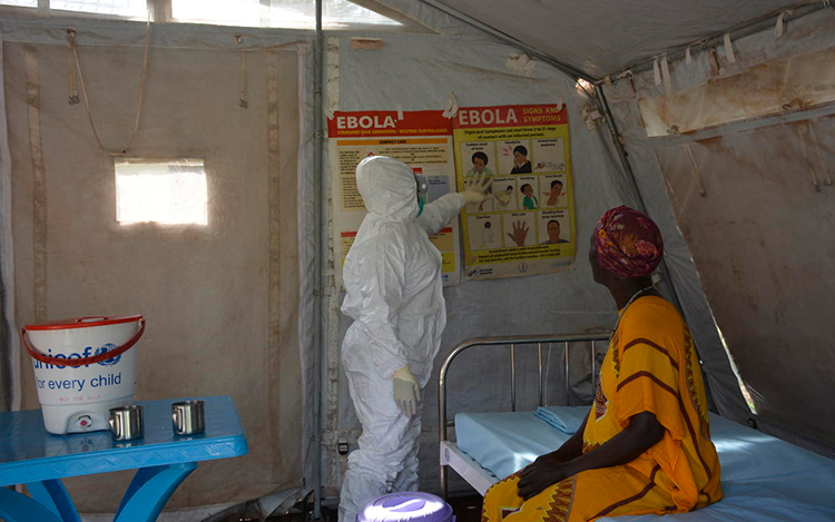 A woman wearing a white hazmat suit helps educate a patient about Ebola in a South Sudanese health facility.