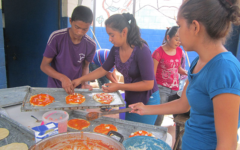 Three young people making mini pizzas.