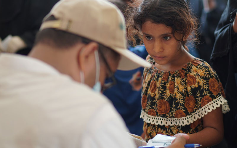 In Yemen, an adolescent girl shows a document to an aid worker who is wearing a mask.