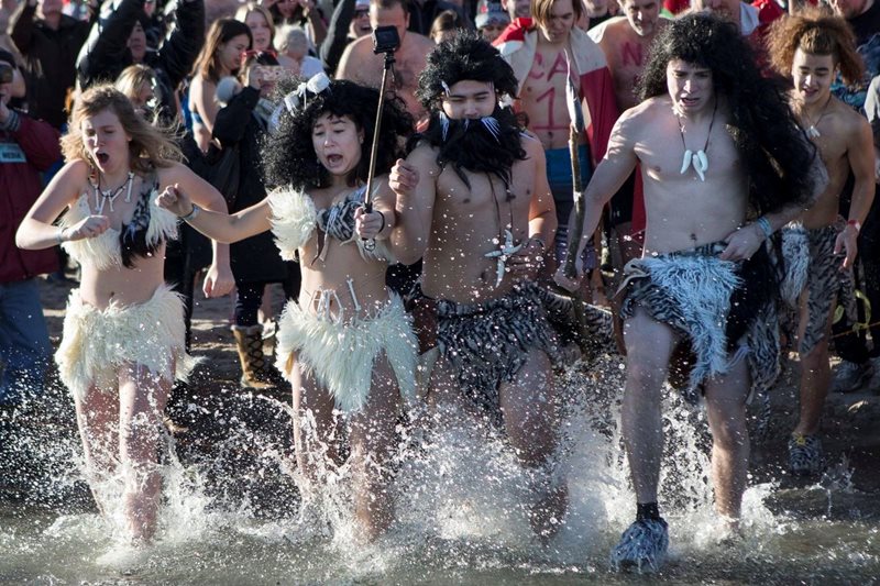 Two women and two men wearing costumes run into a lake as a crowd watches them.