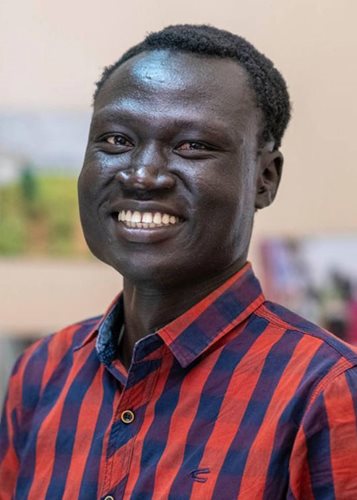 Nhial is a young Sudanese man with a wide smile, wearing a blue and red striped polo.