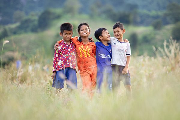 Four sponsored children smiling in a field, with arms around each other.