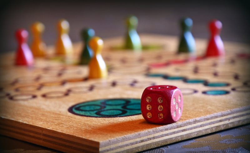 A close-up shot of a wooden game board, red dice and colourful game pieces.