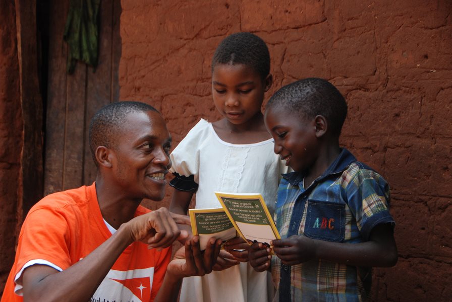 A child ambassador reads a pamphlet with two children.