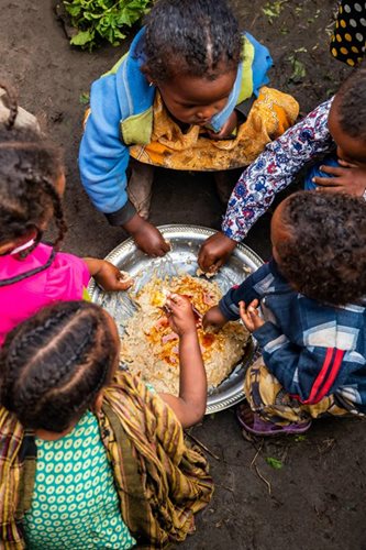 A group of children eat around a common bowl.