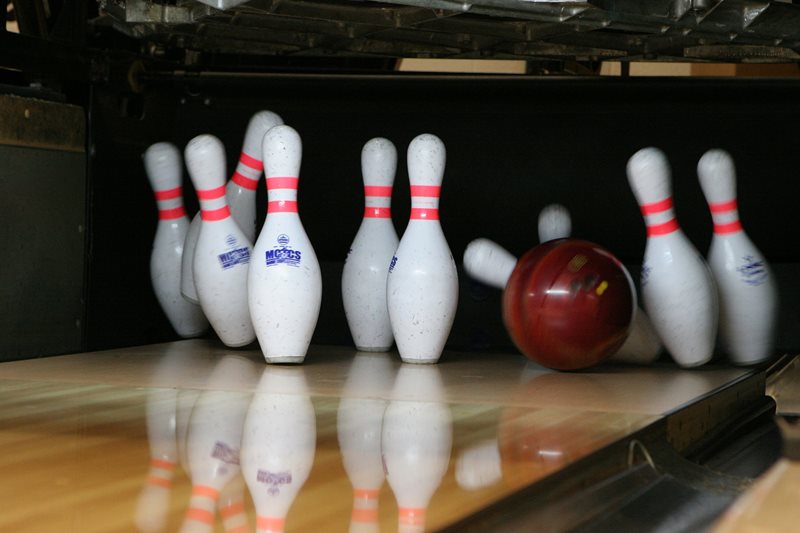 A red bowling balls knocks over bowling pins.
