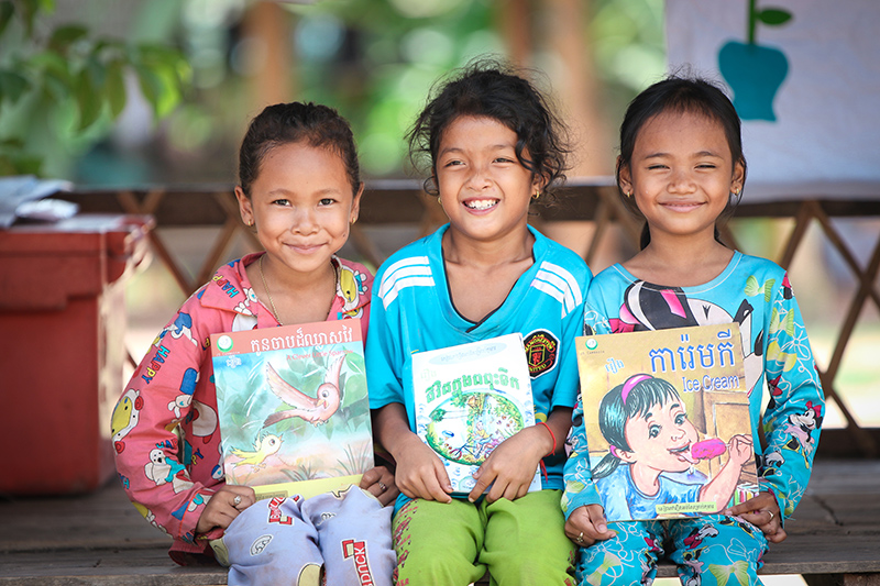 three children holding books and smiling at the camera